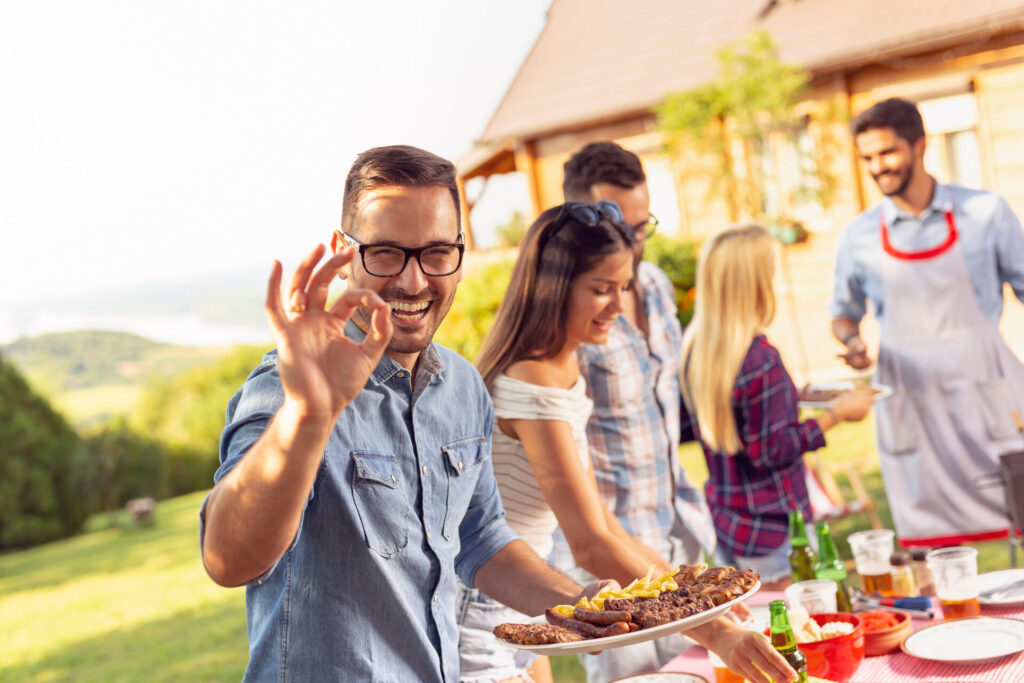 Eine Gruppe von Freunden grillt im Hinterhof, trinkt Bier und hat Spaß an einem sonnigen Sommertag