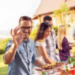 Eine Gruppe von Freunden grillt im Hinterhof, trinkt Bier und hat Spaß an einem sonnigen Sommertag