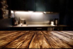 Antiker Holztisch im Vordergrund mit freiem Platz für Dekoration und unscharfer Hintergrund der Küche. 