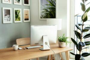 Gemütlicher, leerer Arbeitsplatz für Freiberufler mit Computer, drahtloser Tastatur und Maus auf einem Loft-Holztisch, komfortables Home-Office-Interieur mit grünen Zimmerpflanzen.