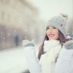 Lächelnde junge Frau in warmer Kleidung bei verschneitem Winterwetter.