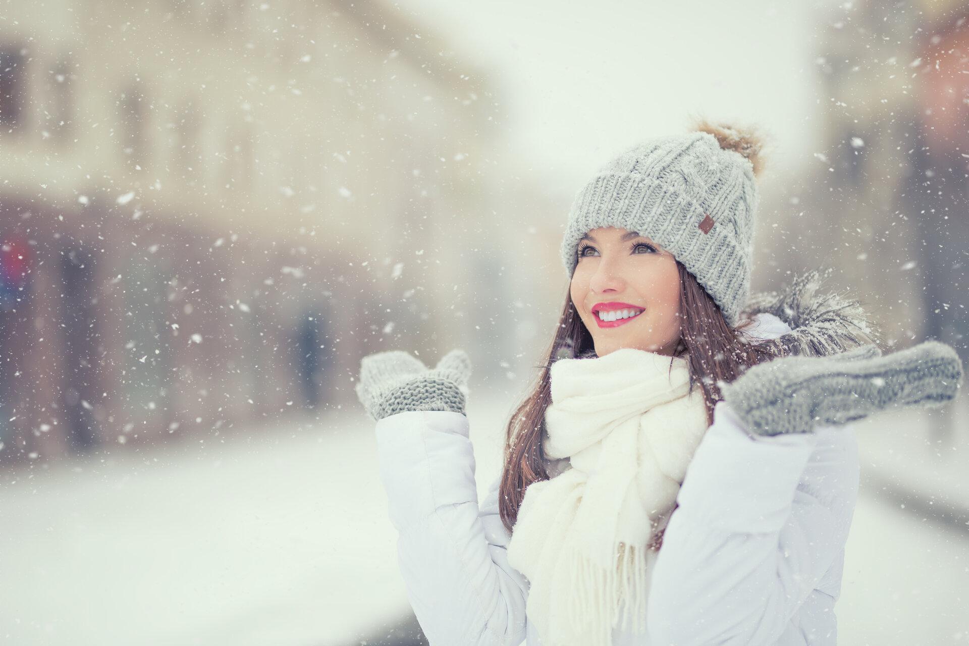 Lächelnde junge Frau in warmer Kleidung bei verschneitem Winterwetter.